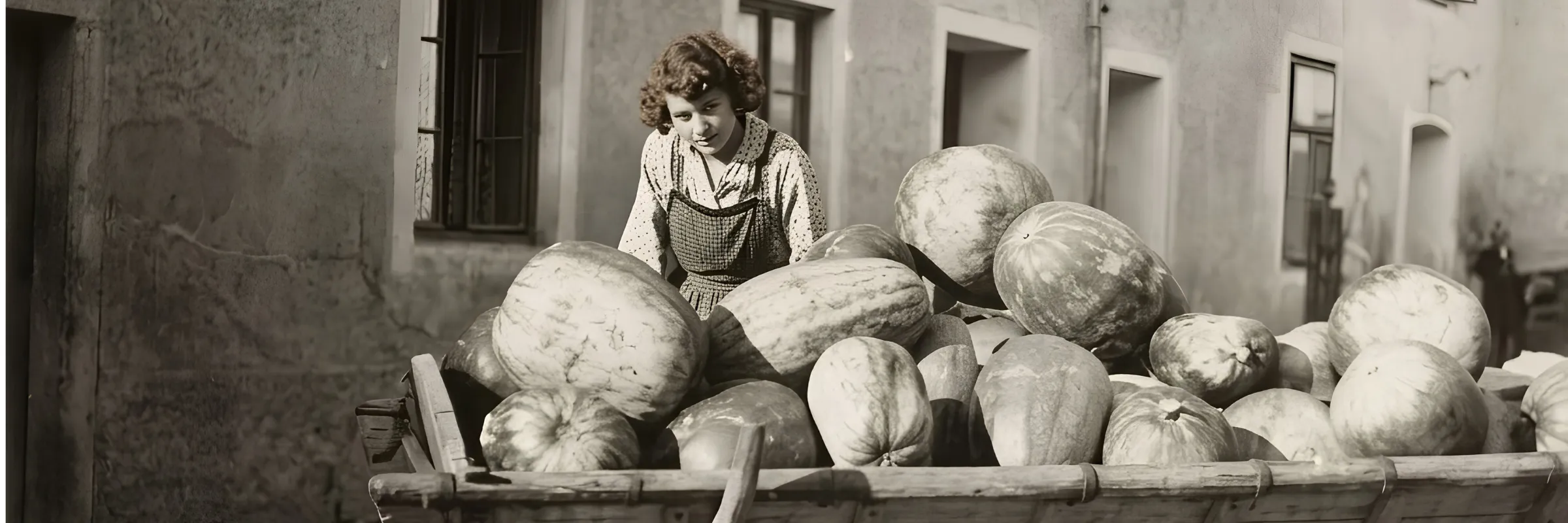Historische Aufnahme aus Maria Anzbach, um 1950: eine junge Frau mit einem Wagen voller großer Kürbisse und Melonen vor einer Hauswand