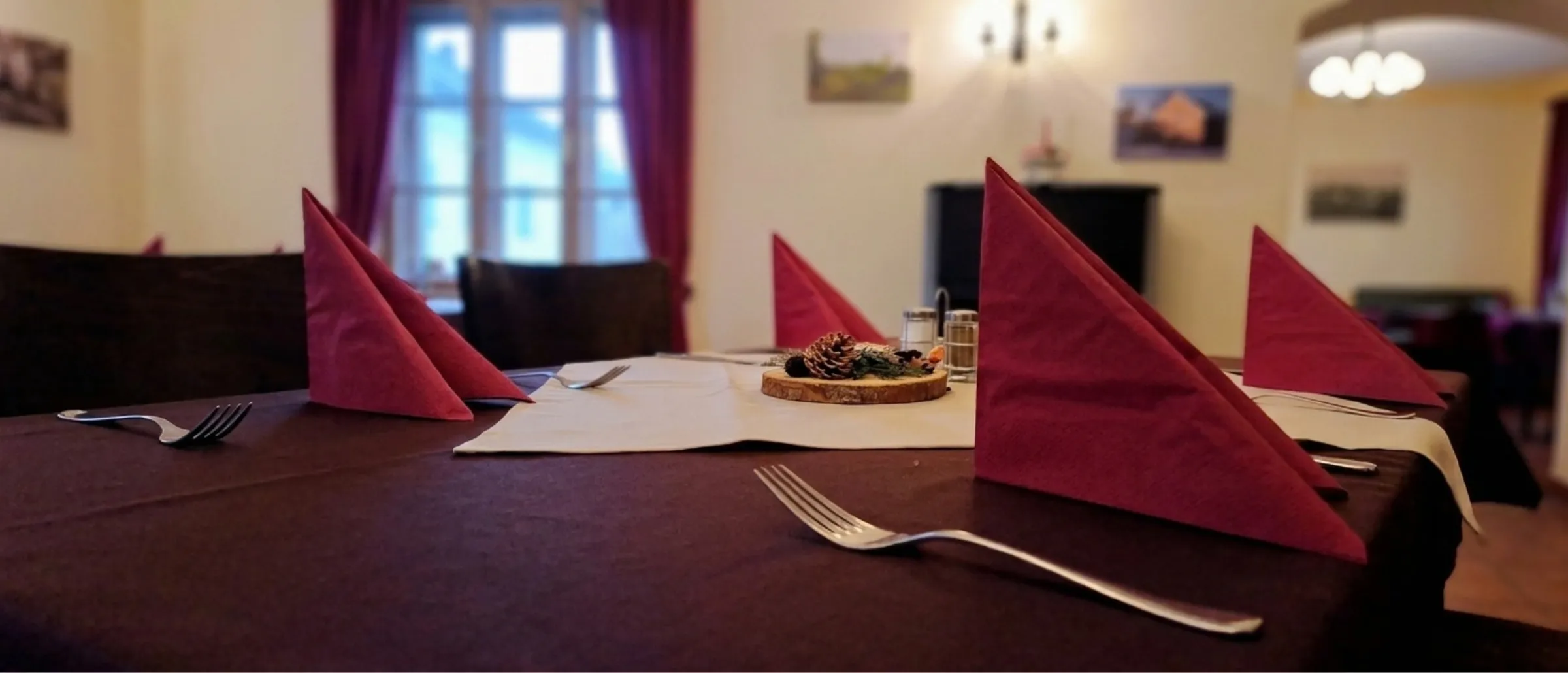 Gedeckter Tisch in der Gaststube mit rot gefalteten Servietten und einer Baumscheibe als Tischdeko