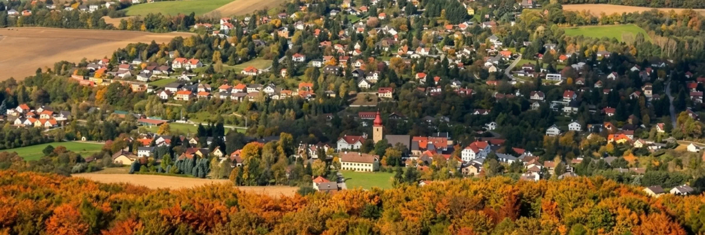 Blick auf Maria Anzbach mit Kirchturm, umgeben von herbstlich gefärbten Wäldern und Feldern im Wienerwald